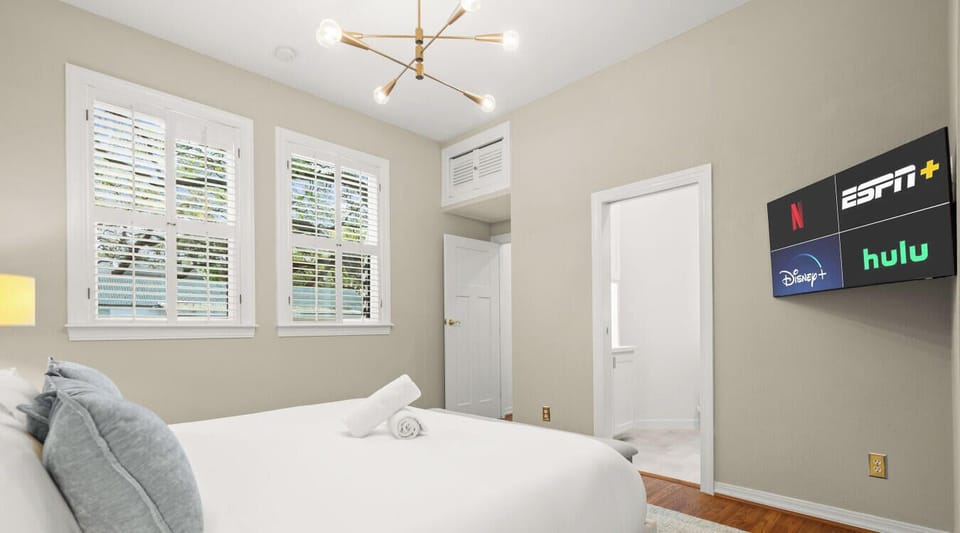 A serene bedroom with streaming-ready TV, tall windows, and direct access to the ensuite bath.
