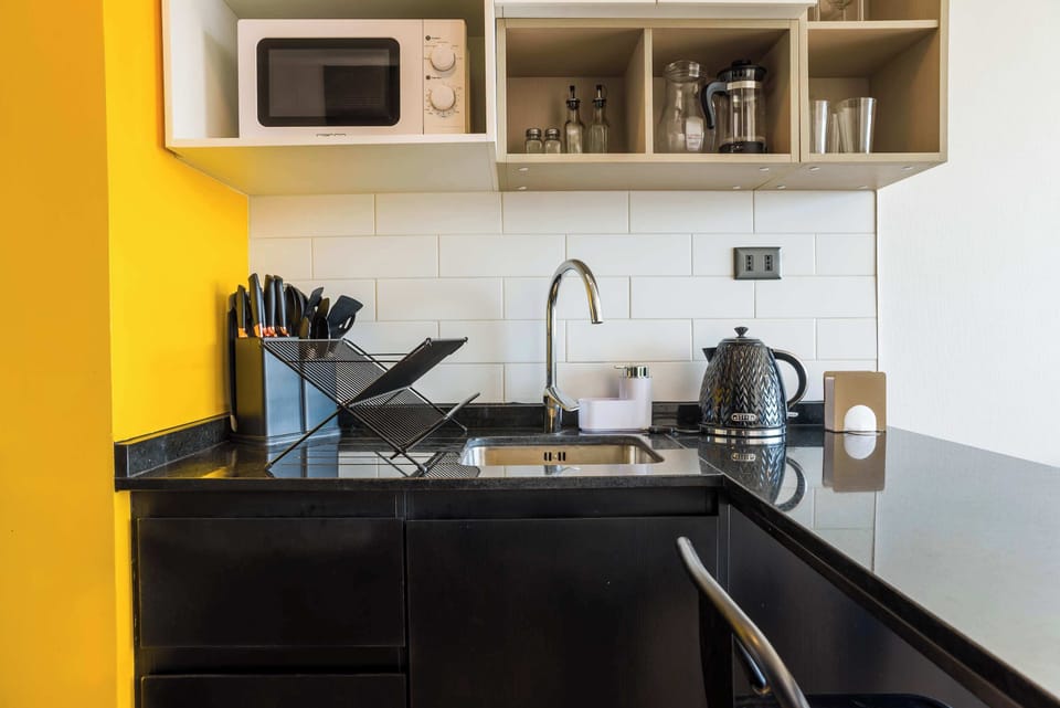 Modern kitchenette with sleek black countertops and vibrant yellow accents, perfect for quick meals and morning coffee.