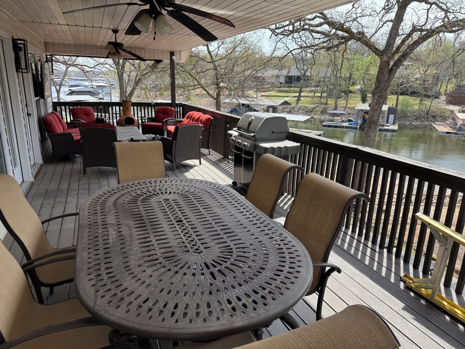 Covered lakeside deck with dining set, grill, and cushioned seating with views