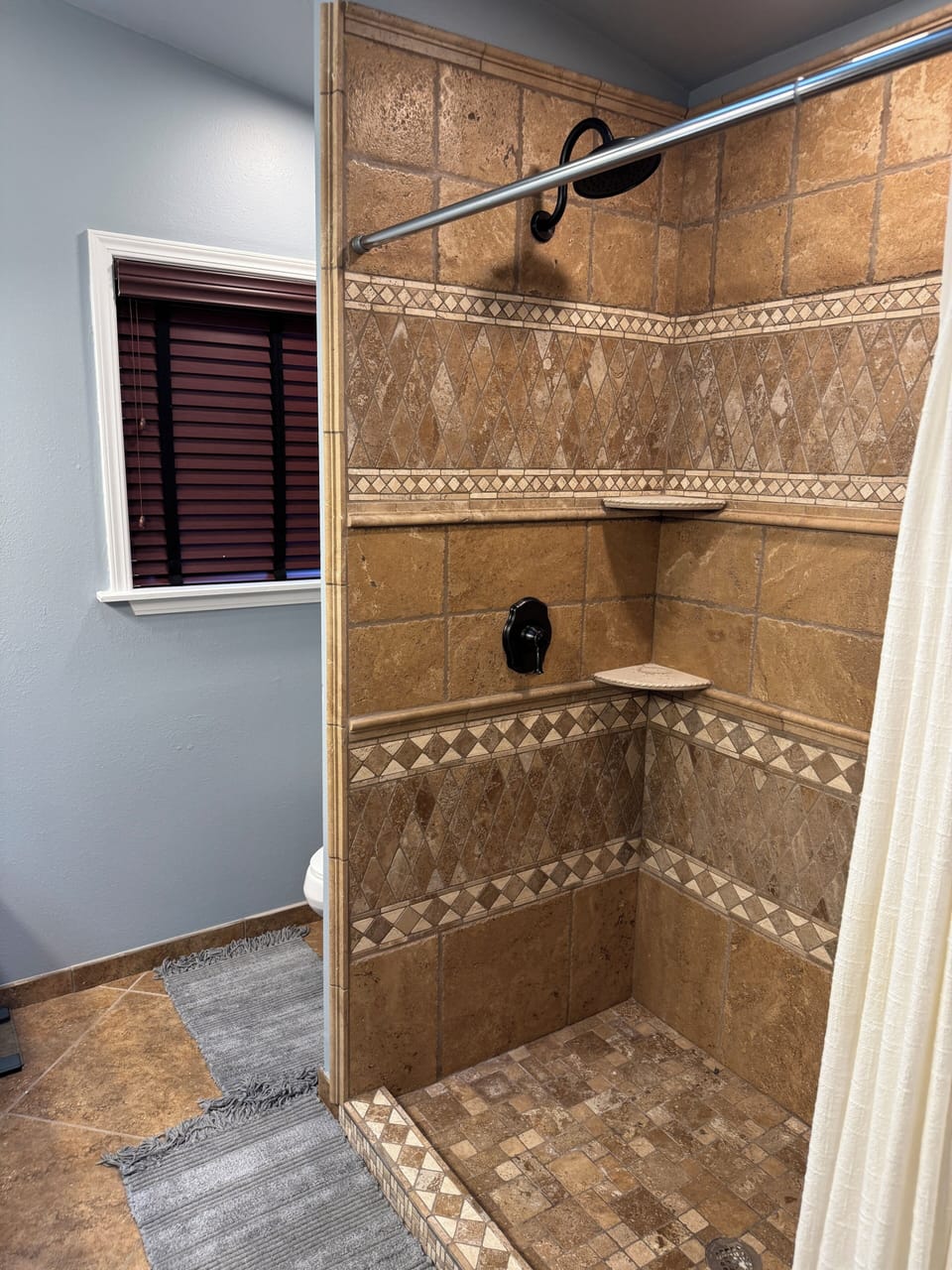 Spacious stone walk-in shower with mosaic accents, shelves, and bronze fixtures