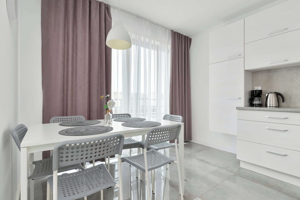 The dining area is set for four people, showcasing grey placemats on a white table and elegant, modern chairs.