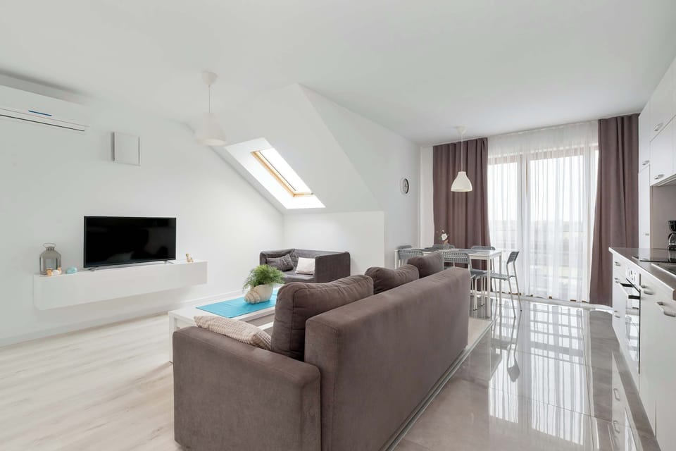 A perspective from behind the sofa highlights the spaciousness of the living room, leading towards large balcony windows that let in natural light.