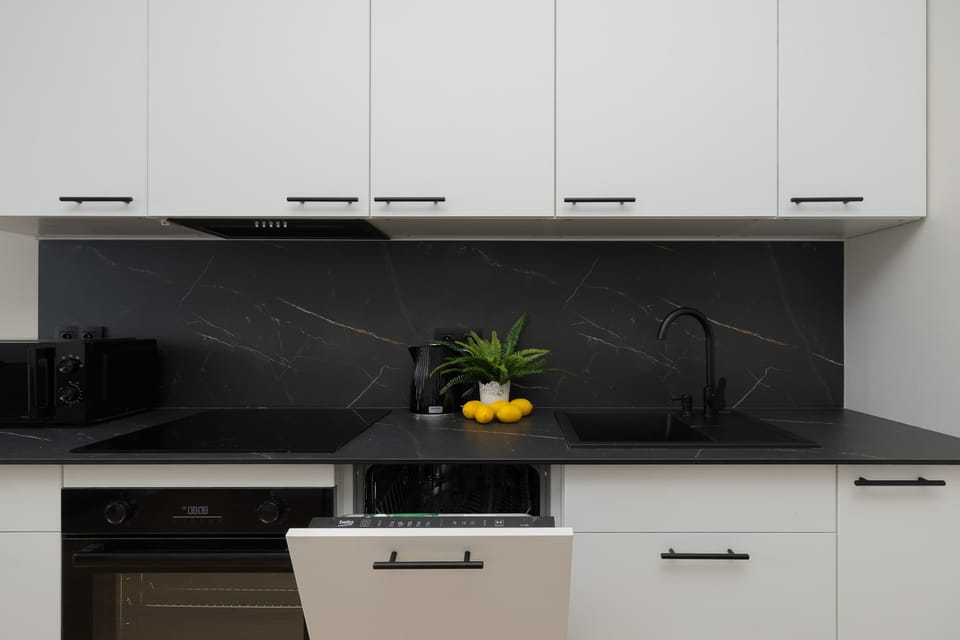 Another angle of the kitchen with white cabinets and black countertops. Appliances are integrated neatly into the design. The space looks practical and well-maintained.
