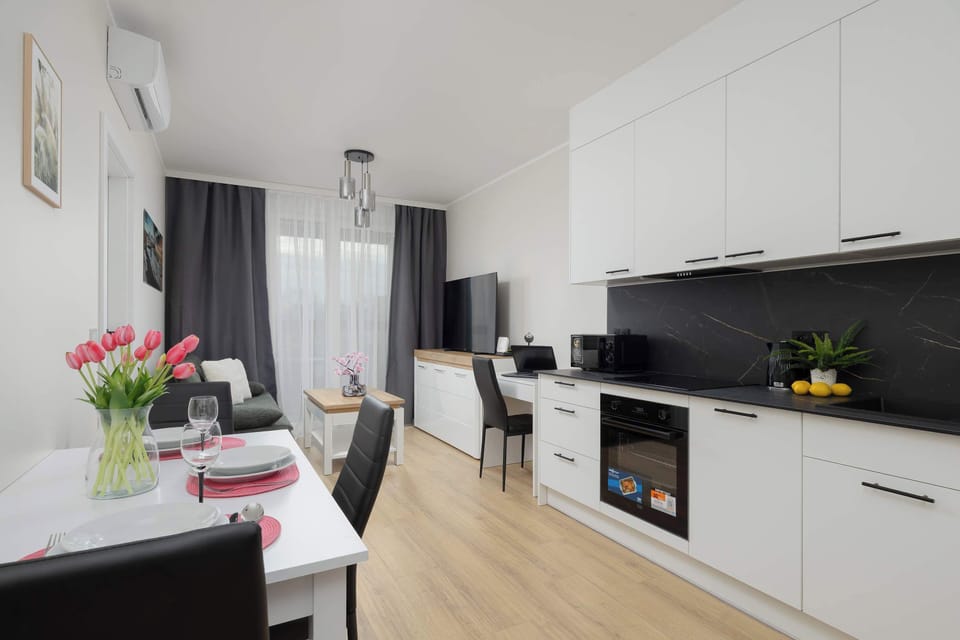 A bright kitchen with white cabinets and black countertops. Small decorative elements like flowers add color to the space. The layout is simple and functional.
