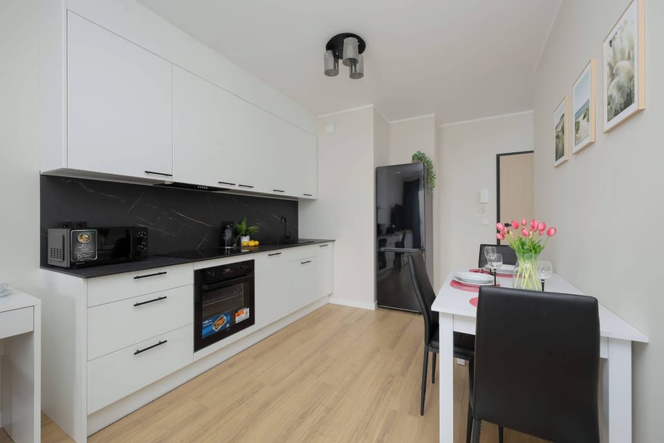 A sleek kitchen counter with built-in appliances and a black backsplash. A small plant decorates the surface. The design is modern and uncluttered.