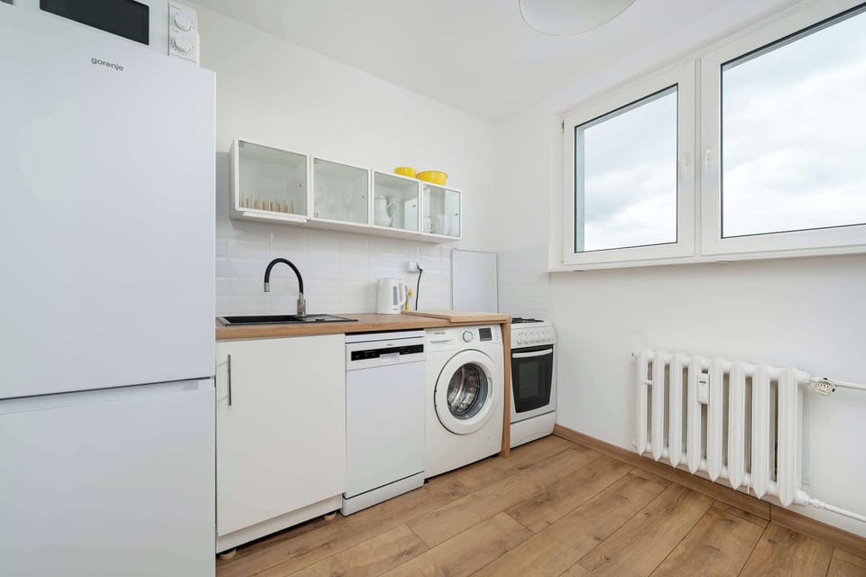 A functional kitchen view with white cabinetry, a countertop workspace, and essential appliances including a washing machine. The arrangement is practical and easy to navigate. Light tones and simple finishes keep the space visually consistent.