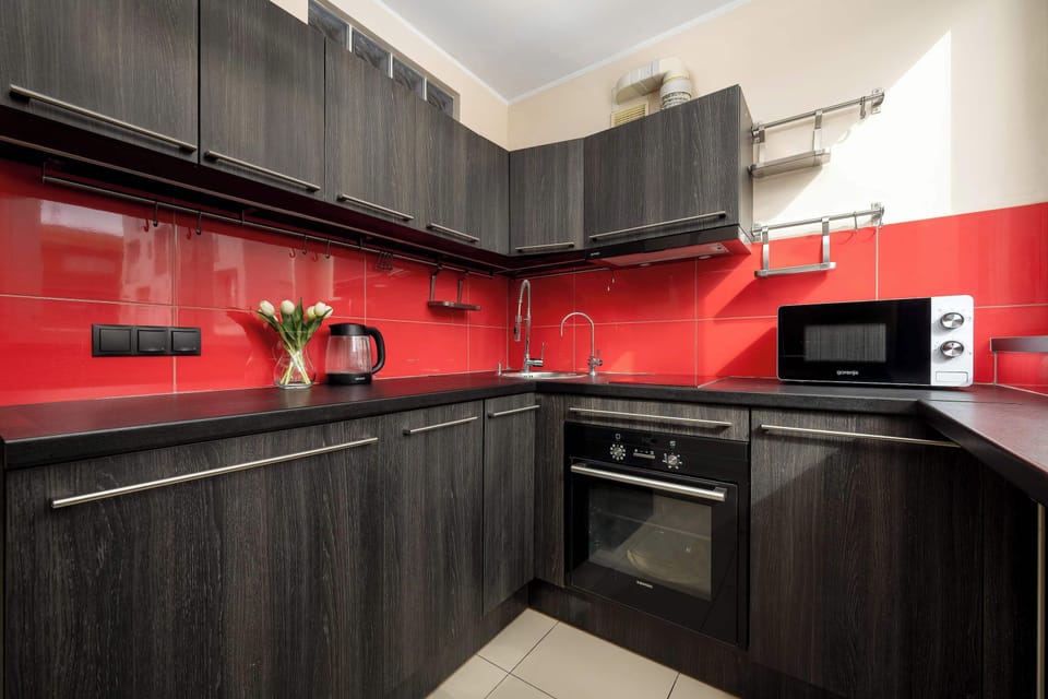 A bold modern kitchen showcases dark wood-textured cabinets contrasted against a vibrant red glass backsplash.