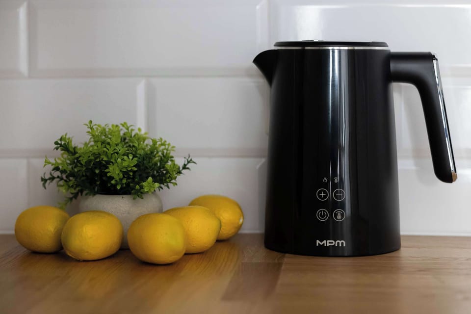 A simple kitchen countertop with a kettle and fresh lemons.