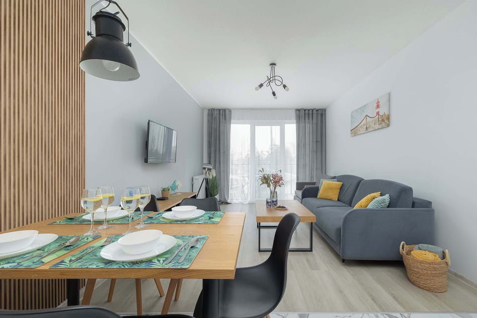 A wooden dining table is set for a meal with elegant tableware, positioned under a modern black pendant lamp.