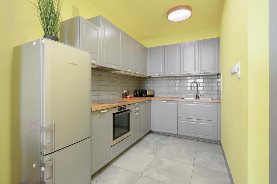 A streamlined and contemporary kitchen with floor-to-ceiling grey cabinets, a sleek built-in oven, and white subway tile backsplash, complete with a stainless steel sink.