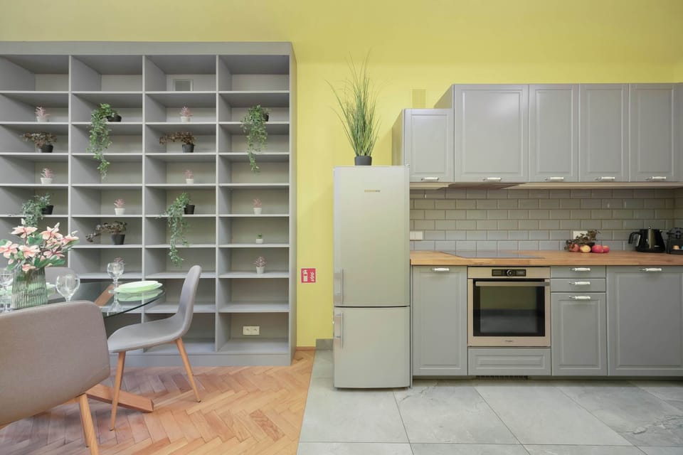 A clean, efficient kitchen space featuring grey cabinetry, a free-standing refrigerator, a built-in oven and microwave, and open grid shelving for a modern feel.