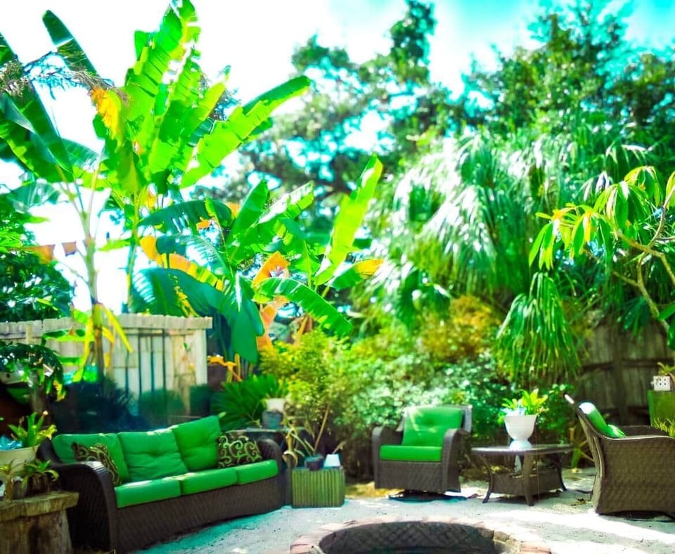 At Fennario Resort, enjoy at tropical oasis on the mini beach with lush plants, banana trees, and palms. Cozy wicker furniture with green cushions surrounds a central fire pit, offering a relaxing space to unwind. 