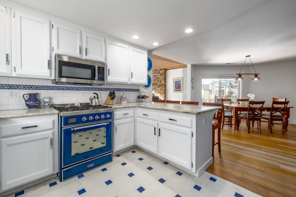 Kitchen view with range, microwave, peninsula, dining table, fireplace, and main living spaces in sight.