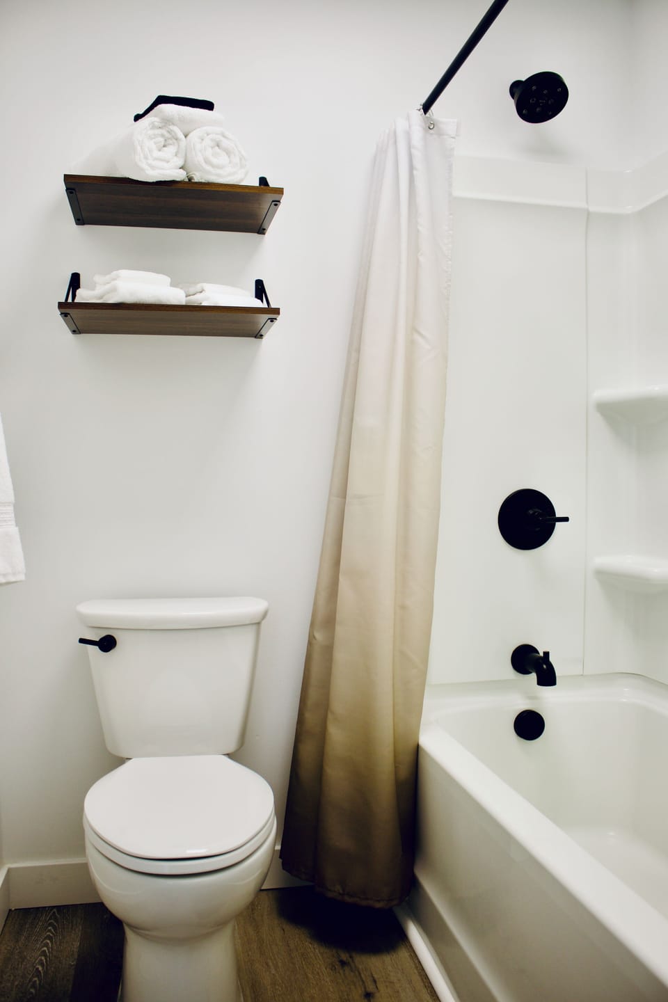 Modern bathroom with black fixtures, tub shower, and stocked towel shelves