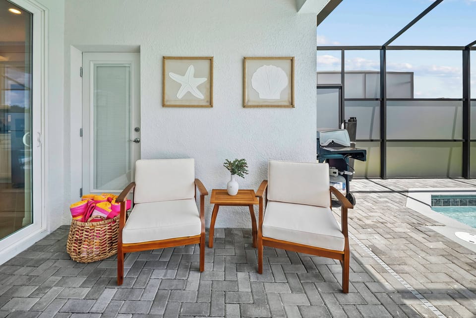 Step outside to a lovely seating area with two light chairs and a wooden table, ideal for morning coffee or evening relaxation, while framed coastal artwork enhances the beach-inspired decor, inviting you to unwind.