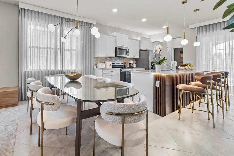 Welcome to a bright and stylish kitchen and dining area with large windows, sleek white cabinetry, and elegant lighting. The chic round dining table and comfortable seating invite you to enjoy meals and great conversations.
