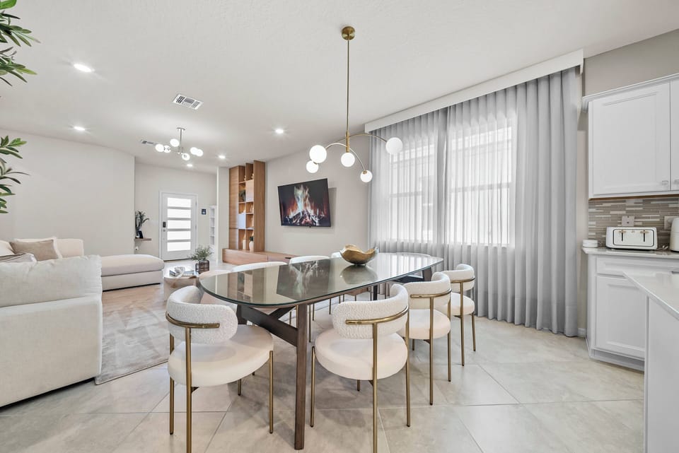 Experience a chic dining area with sleek round chairs and a polished glass table, perfect for gatherings. The warm glow from modern pendant lights enhances the light decor, making it a bright and welcoming space for shared meals.