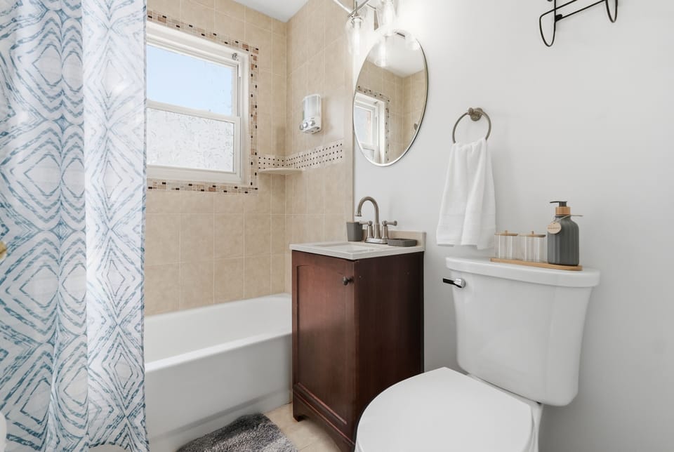 Bright full bathroom with tub, shower, and fresh towels.