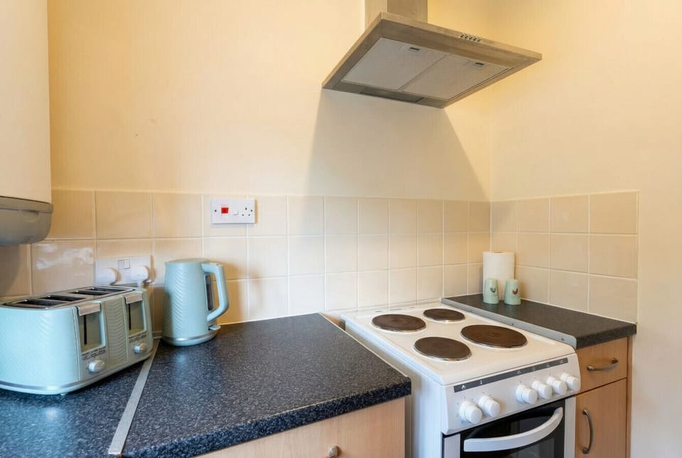 The retro sage toaster and kettle beside a four-ring cooker give the kitchen its cheerful personality.