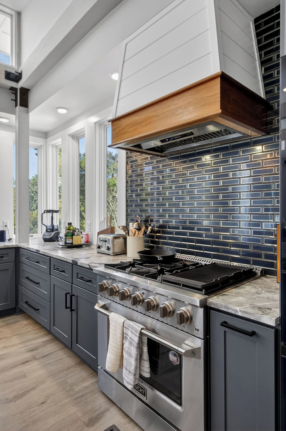 Bright chef’s kitchen with a large marble island and modern blue‑gray cabinetry.