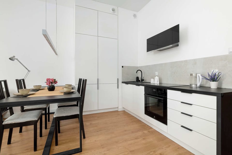 The dining area is shown next to the kitchen, featuring a black table and matching chairs. A tall, white built-in cupboard provides ample storage space behind the dining set.