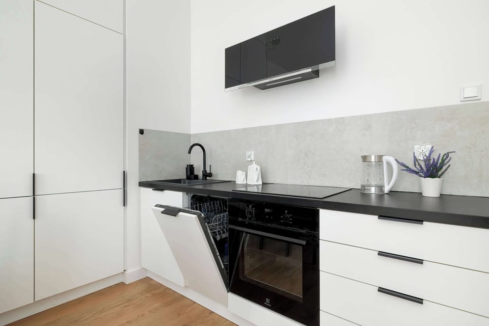 The kitchen is shown from a wider angle, revealing the seamless integration of the appliances into the cabinetry. A dark backsplash protects the wall behind the sink and stove area.