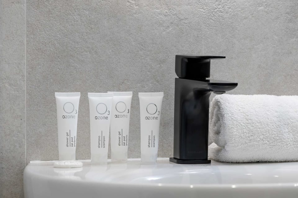 A black faucet is the focal point of this bathroom detail, accompanied by small white amenity bottles. A fresh white towel is folded nearby, emphasizing the cleanliness of the vanity area.