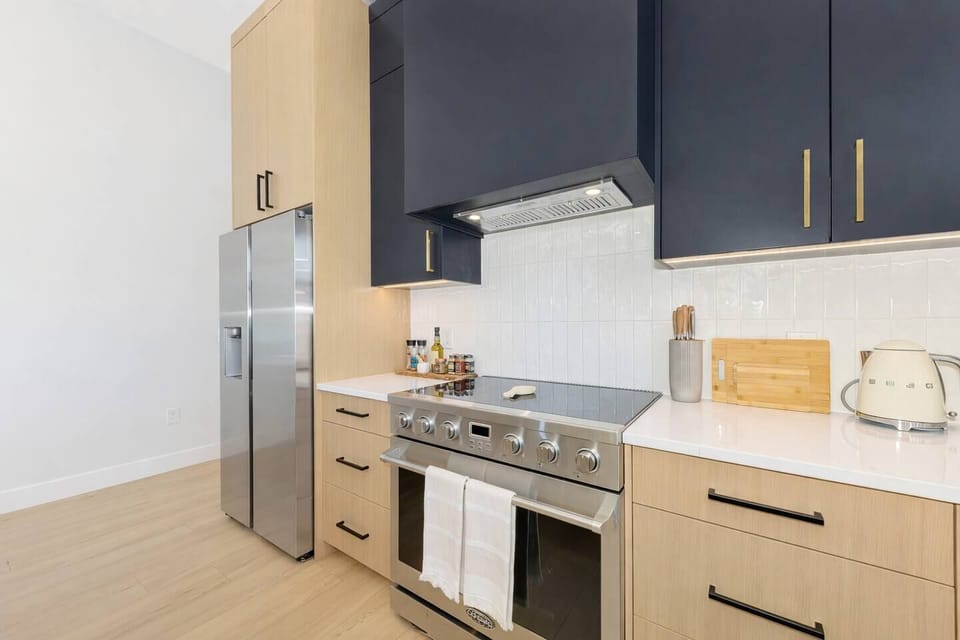 Large fridge, stove and oven. Knives, cutting board, water kettle and microwave to the right of stovetop. Spice rack to the left.