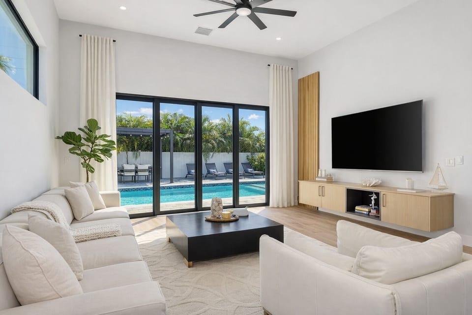 Bright and modern Sarasota living room with floor-to-ceiling glass doors opening to a private pool. Relax on the comfy sectional, stream on the Smart TV, and enjoy seamless indoor-outdoor living near Siesta Key and downtown Sarasota.