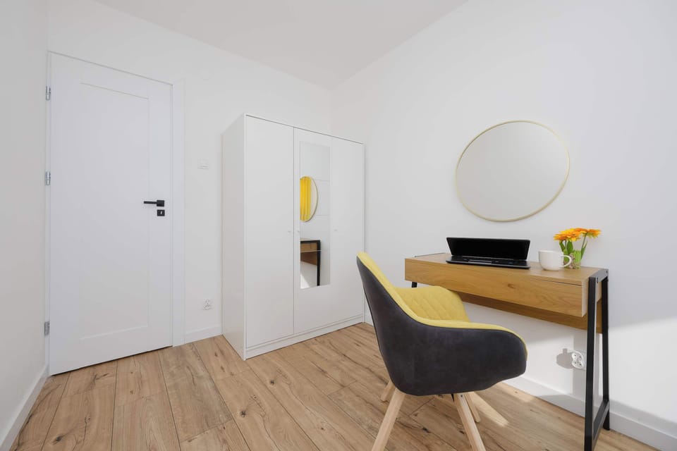 Bedroom area with a desk, chair, and round mirror. The space is minimal and bright.