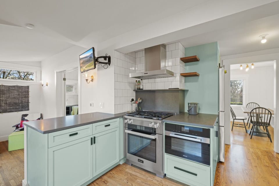 Mint-green cabinets, wood shelves, and a dark tile backsplash pair with a professional gas range for a sleek, chef-inspired finish.