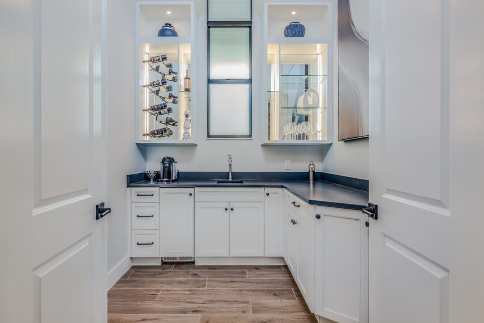 Coffee and beverage bar with sink, illuminated display shelving, wine storage, glassware, and complimentary coffee station.