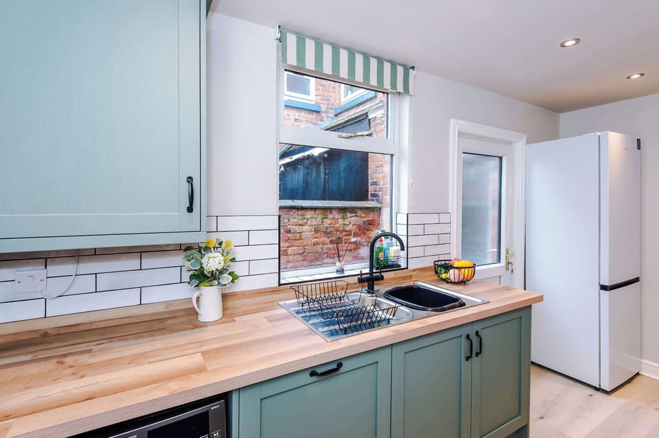 A bright, organized kitchen with gray cabinets, wood countertops, white subway tiles, and appliances including a microwave, toaster, and kettle, accented by a fire safety sign and recessed lighting for a modern touch.