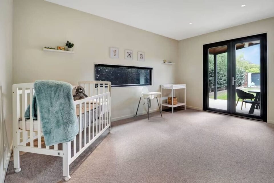 Light-filled nursery featuring a cot, highchair, soft neutrals, and access to the outdoor area at Banksia House High Country Retreat in Mansfield Victoria.