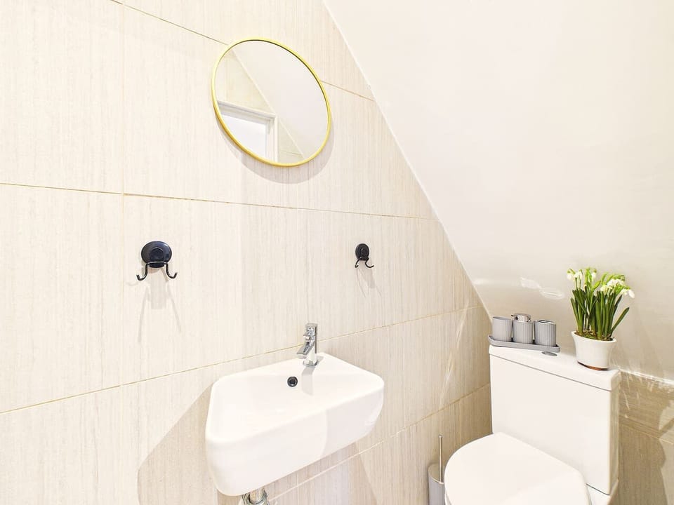 A brightly lit, compact ensuite featuring an efficient corner sink with a chrome faucet and a dedicated wall-mounted electric shower.