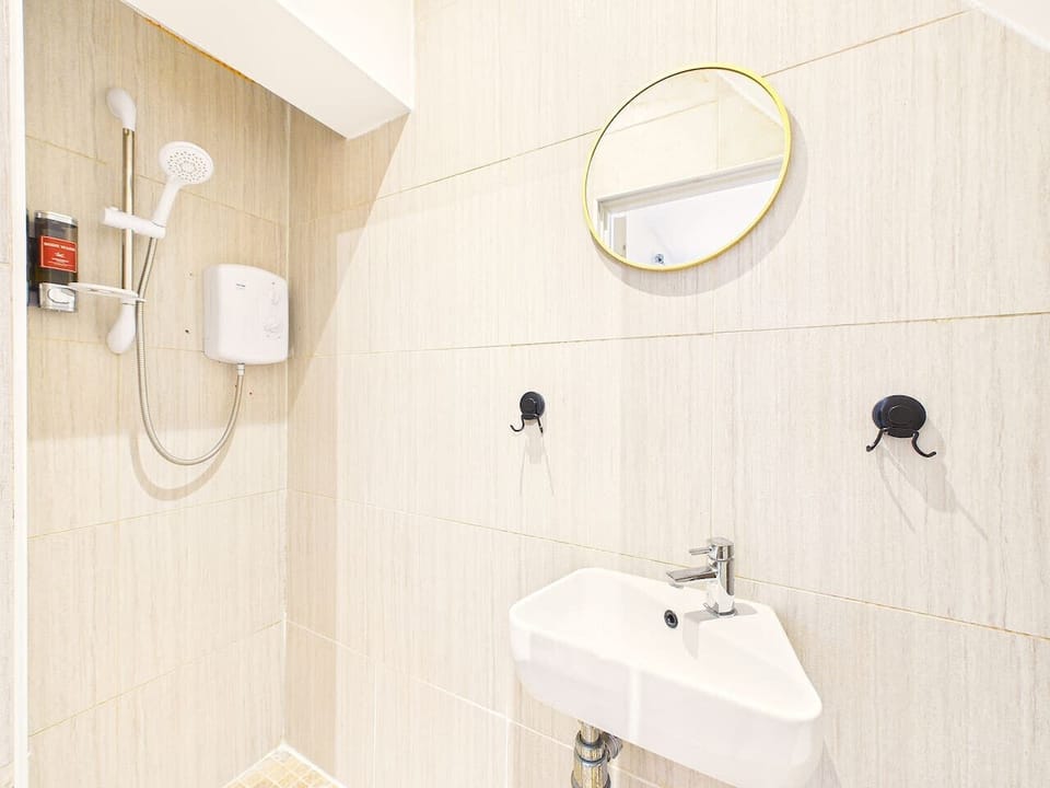 A brightly lit, compact ensuite featuring an efficient corner sink with a chrome faucet and a dedicated wall-mounted electric shower.