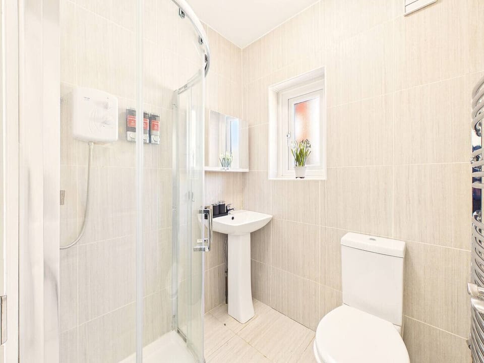 It boasts a curved glass corner shower, a classic white ceramic pedestal sink and a mirrored medicine cabinet is mounted directly above the sink, providing hidden storage.