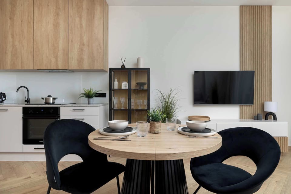 A dining corner with a round table and stylish upholstered chairs placed next to a compact kitchenette. Wooden finishes and soft lighting enhance the cozy and modern feel.