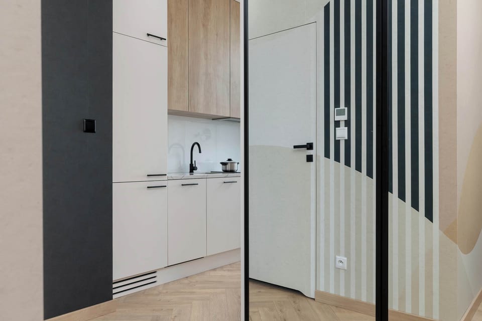 A compact hallway leading into a kitchenette area, designed with clean lines and modern cabinetry. Light colors and simple finishes make the space feel neat and well-organized.