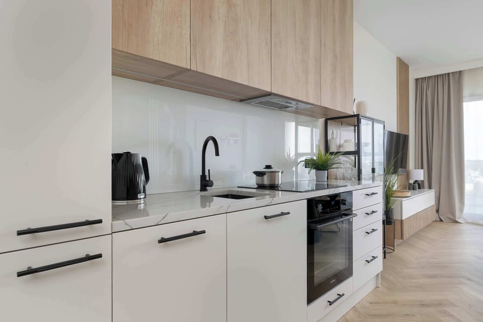 A modern kitchenette with sleek white cabinetry and a long countertop, equipped with built-in appliances. The minimalist design is complemented by light wood accents and under-cabinet lighting for a clean, functional look.