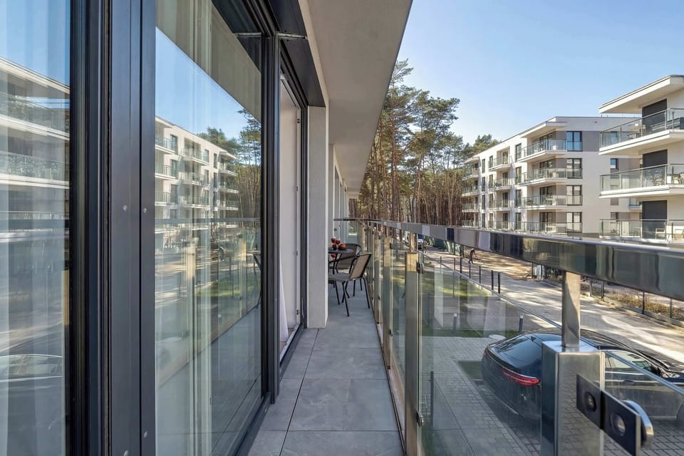 A perspective of the long balcony walkway with views of the surrounding pine forest and neighboring modern buildings.