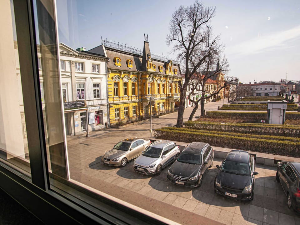 Another window view shows a wider perspective of the street, including colorful buildings and several parked cars. The scene feels lively yet relaxed, with plenty of daylight.