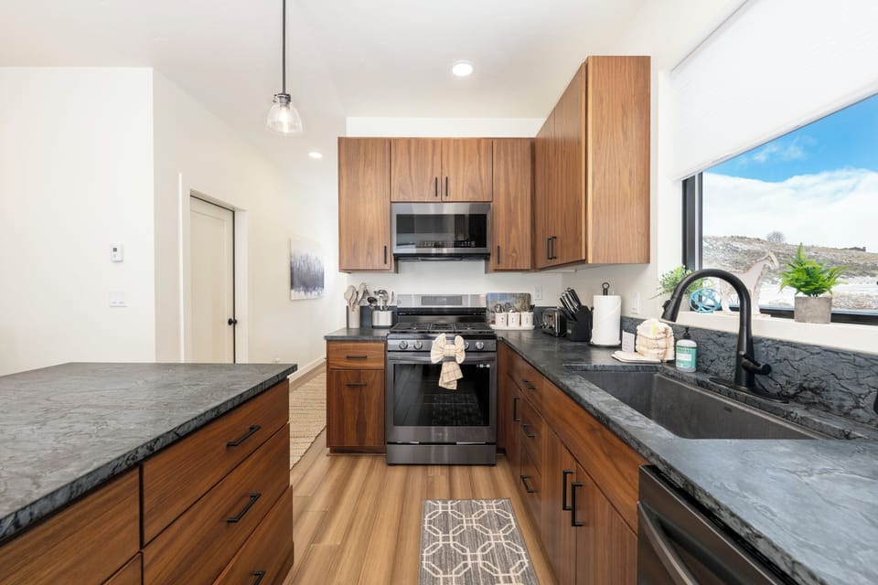 Your modern kitchen at Base Camp Townhome 106 features sleek wood cabinets, granite countertops, and stainless steel appliances with stunning mountain views.