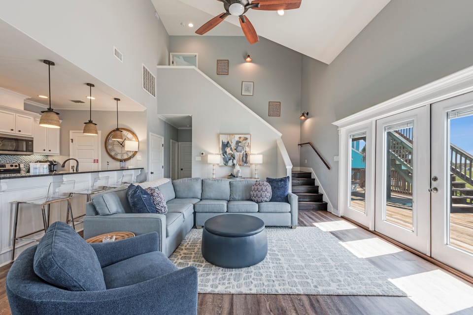 Relax in your spacious living room featuring plush sectional seating, soaring ceilings with exposed beams, and natural light streaming through French doors.