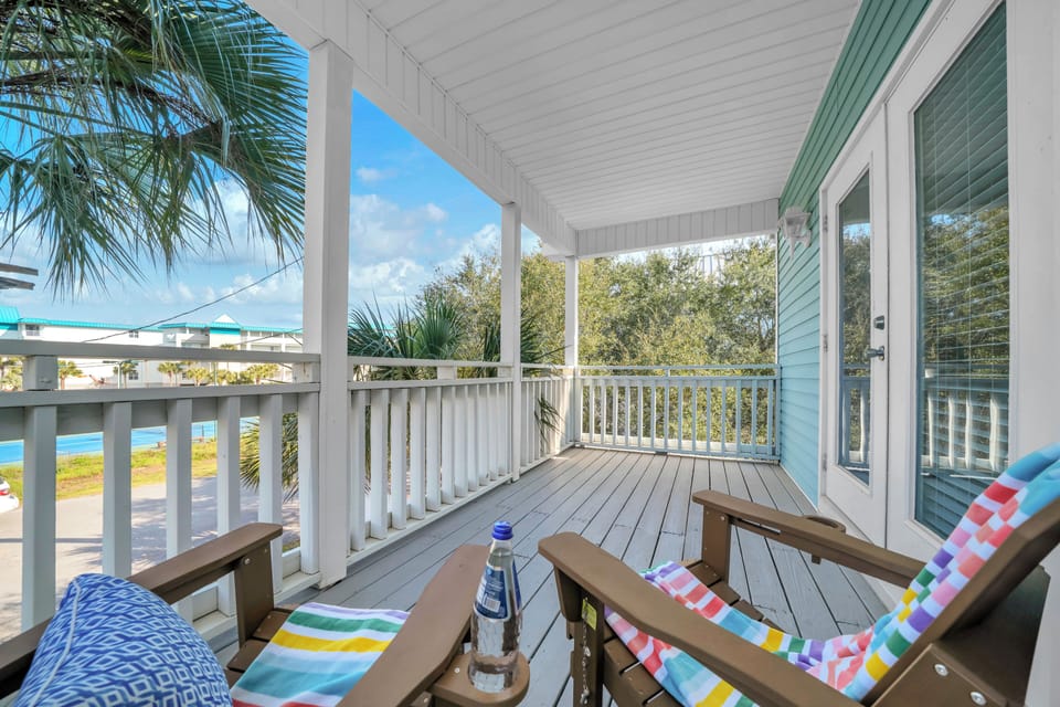 Relax on your private covered deck with colorful beach chairs, enjoying tropical breezes and glimpses of the nearby coastline through swaying palms.
