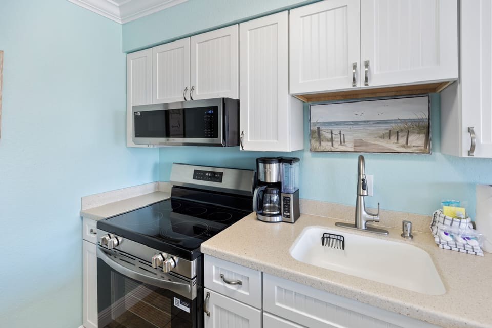 Your coastal-themed kitchen features modern appliances and charming beachscape artwork, perfect for preparing meals with ocean-inspired ambiance.