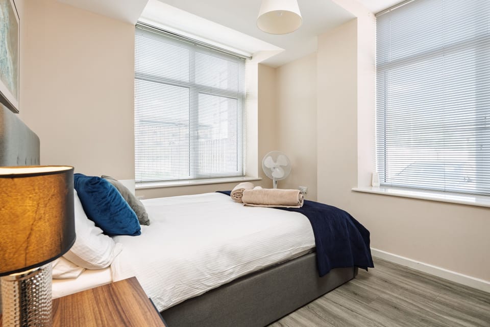 Bedroom two across the bed to its two windows, with a portable fan on the sill