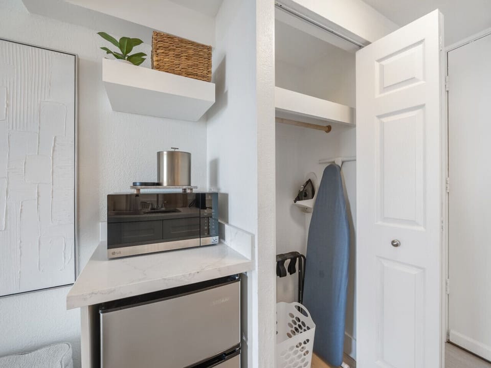 Storage closet with iron, ironing board, luggage rack and laundry basket