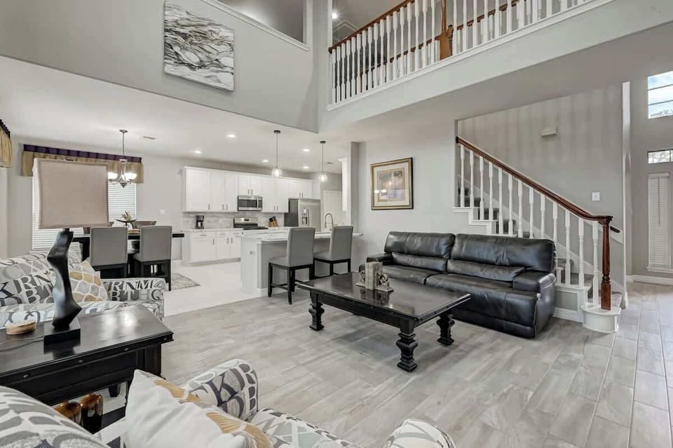 Spacious main living space featuring leather seating, elegant staircase, and open flow to the dining area.