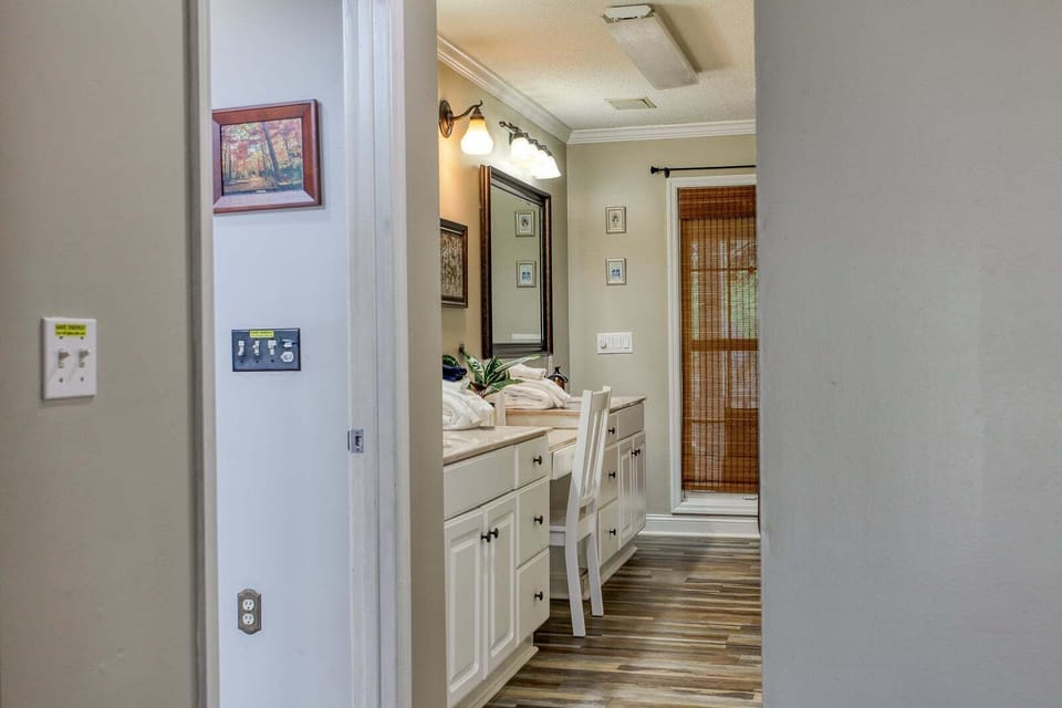 Bathroom vanity with a large framed mirror, white cabinetry, and visible doorway leading into the cabin interior. This bright bathroom space offers convenient access to shared living areas in the Bryson City cabin.